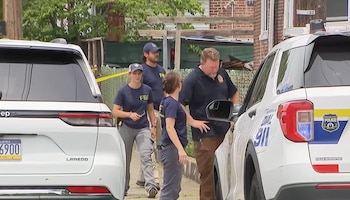 Agentes con vestimenta del FBI y personal policial caminan entre dos vehículos junto a una propiedad acordonada con cinta amarilla