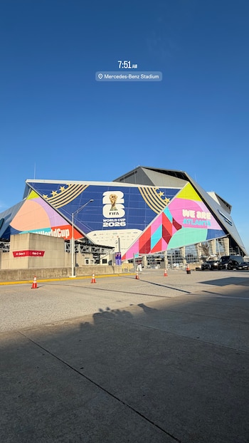 Fachada exterior del Estadio Mercedes-Benz con banners de la Copa Mundial de la FIFA 2026, varios vehículos y conos de tráfico en el acceso