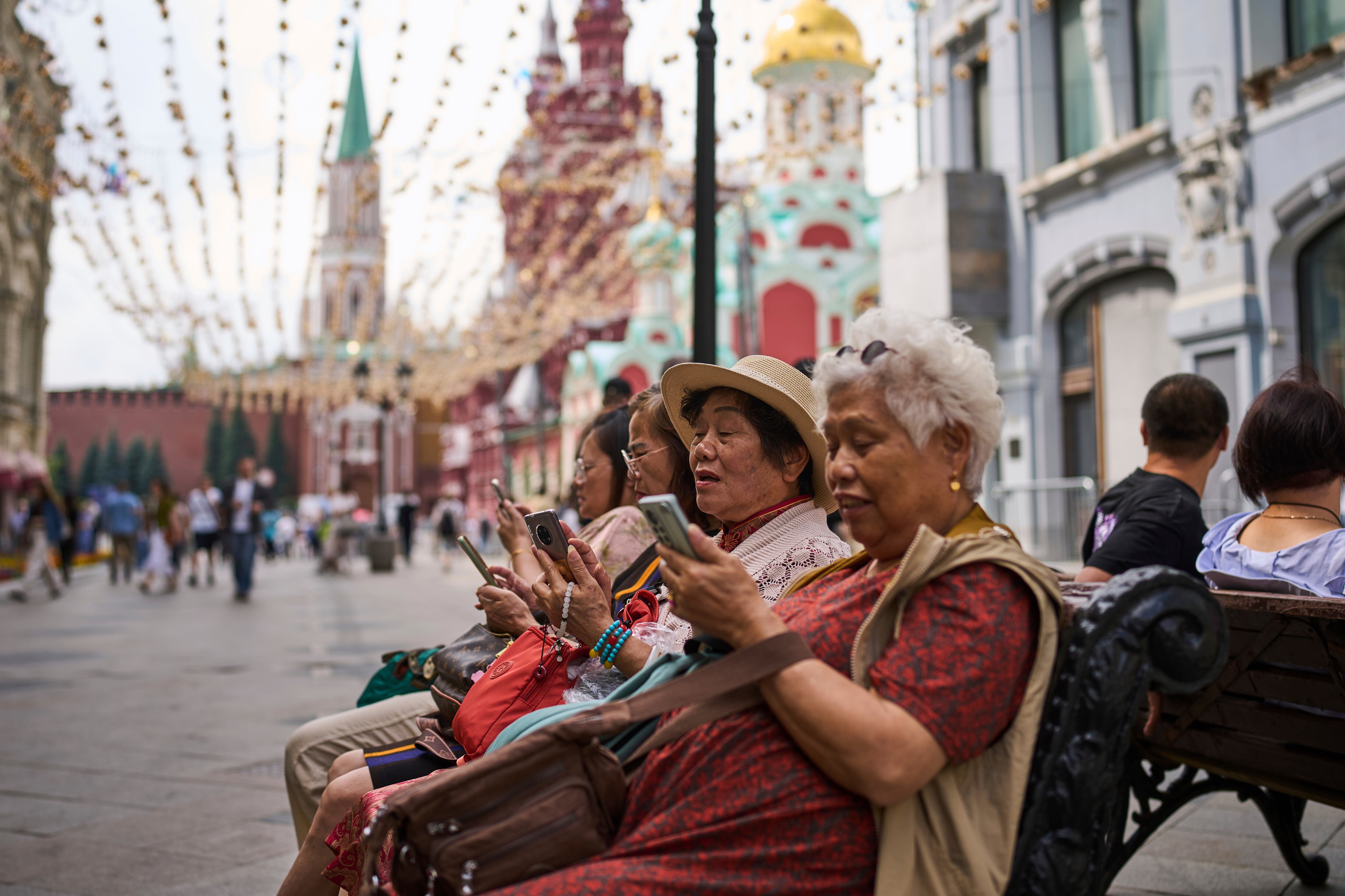 Turistas sentados cerca del Kremlin en Moscú consultan sus teléfonos. (Foto AP/Alexander Zemlianichenko)