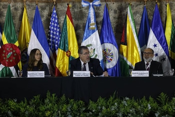 Un grupo de asistentes posa de pie alrededor de mesas en forma de U dentro de un salón con techo de madera y una pantalla frontal