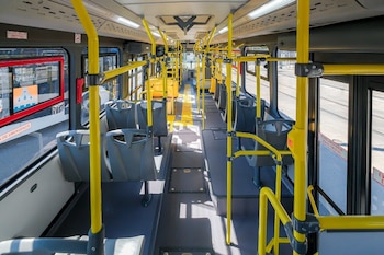 Interior de un autobús moderno y vacío con asientos grises y pasamanos amarillos vibrantes. El pasillo central es amplio y luminoso