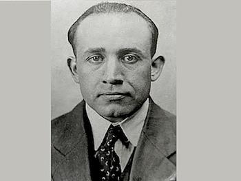 Fotografía en blanco y negro del busto de un hombre adulto con traje oscuro, camisa clara y corbata estampada
