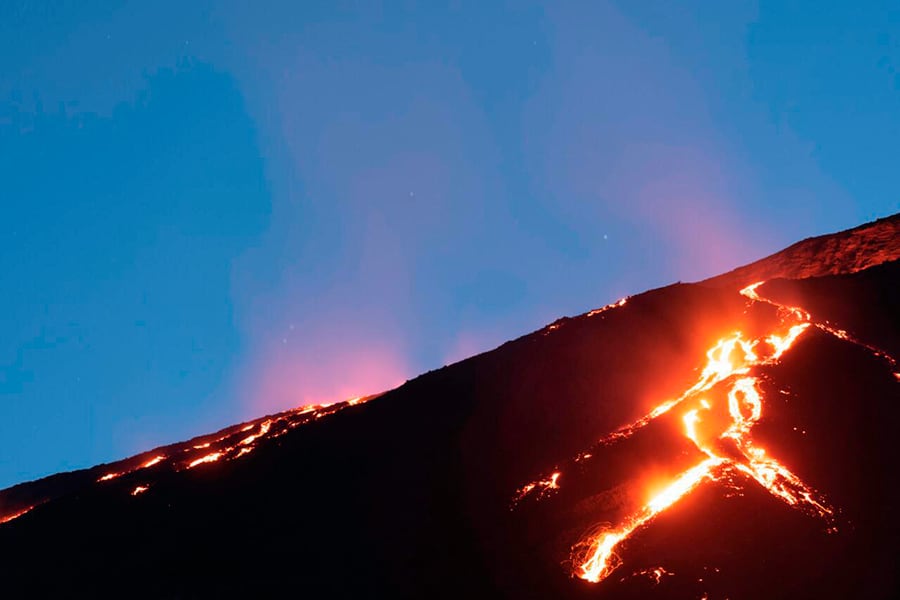 La lava incandescente fluye por la ladera del Volcán Pacaya en Guatemala bajo un cielo azul oscuro al atardecer o amanecer. (Conred)