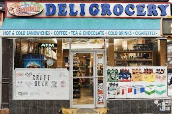 Fachada de una tienda de comestibles con toldo azul, puerta de vidrio central y carteles de cerveza artesanal en el escaparate