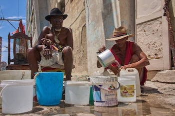 Oscar Joaquín López (izquierda) y su compañero de casa, Wilfredo Cisneros Duarte, recogen agua de una tubería en la calle en La Habana, Cuba, el 7 de septiembre de 2026. (AP Foto/Ramón Espinosa)