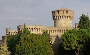 Castillo de piedra con torre circular y muros con arcos, vegetación abundante y un cielo con nubes dispersas