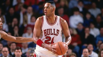 Jugador de baloncesto con camiseta blanca de los Chicago Bulls, número 24, sostiene un balón. Lleva muñequera roja. Público borroso en segundo plano.