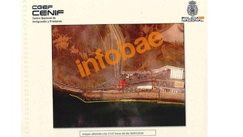 Vista aérea de una zona costera fronteriza con carreteras, un marcador rojo, una línea de puntos amarillos y logotipos oficiales arriba