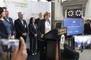 Una mujer habla en un podio del Congreso de la República junto a un grupo de personas y una pantalla digital azul