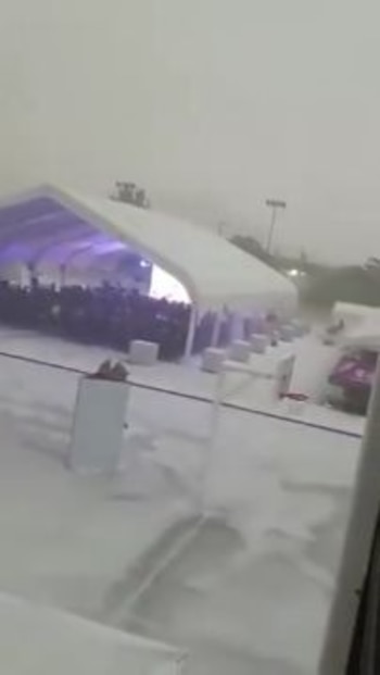 Gran carpa blanca con iluminación púrpura interior, personas en su interior, suelo exterior cubierto de nieve, visibilidad baja