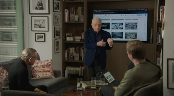 Martin Scorsese, un hombre mayor de cabello canoso, de pie y gesticulando ante una pantalla grande que muestra imágenes. Dos hombres sentados lo escuchan
