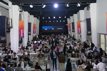 Vista elevada de una sala con personas sentadas en mesas con computadoras, carteles de Santa Fe Business Forum y un escenario al fondo