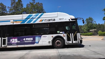 Vista lateral de un autobús blanco de MARTA con franjas azules y naranjas, número 1617, estacionado al aire libre bajo un cielo azul claro