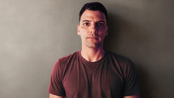 Plano medio de un hombre con el pelo corto y camiseta de cuello redondo que mira fijamente hacia el frente ante una pared lisa