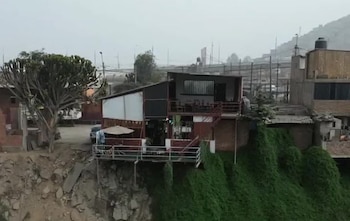 Una casa de dos niveles construida sobre el filo de un terreno colapsado junto a un barranco con vegetación