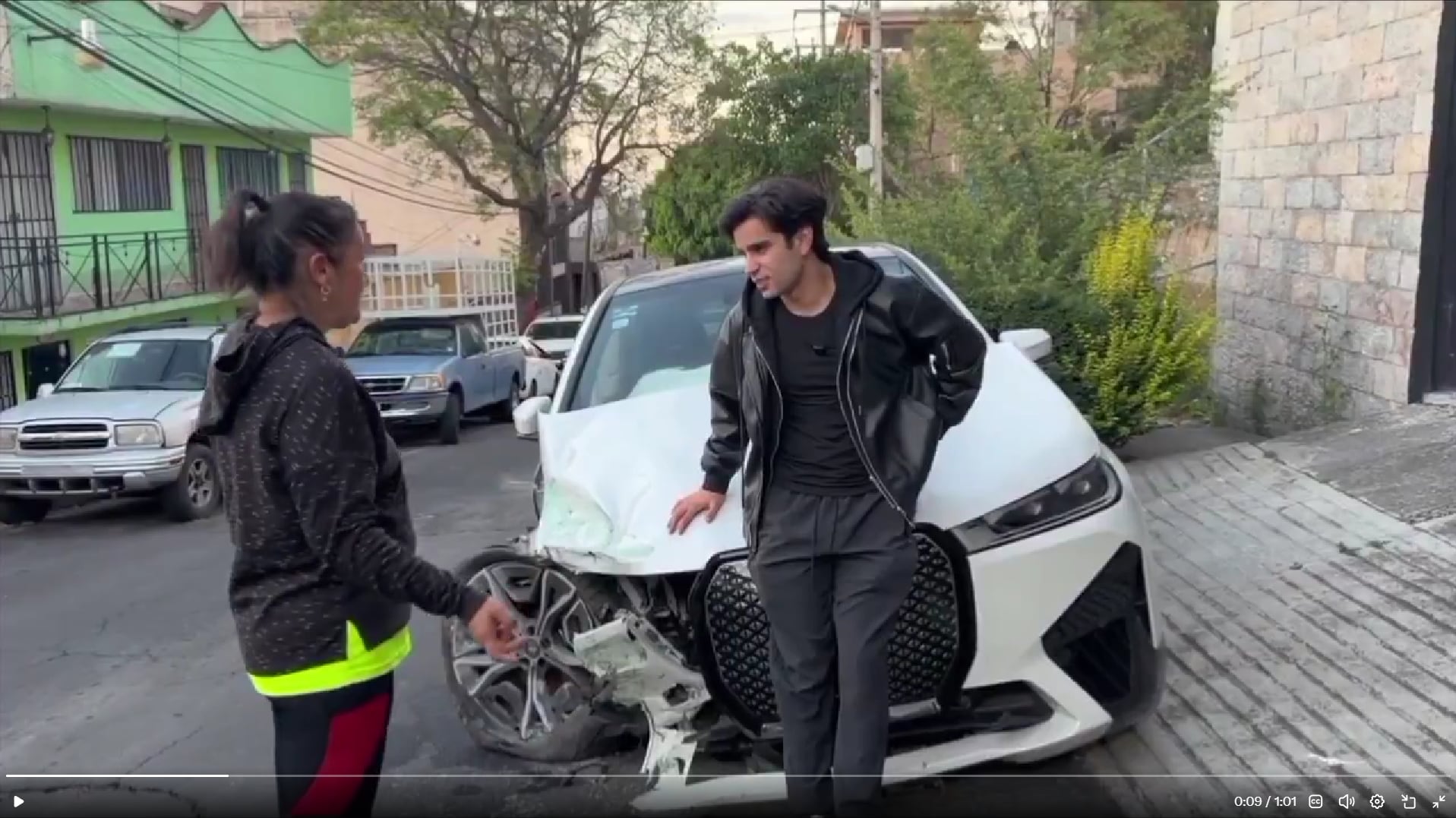 Una mujer se acerca a Aaron Mercury para ofrecerle palabras de aliento junto a su vehículo blanco visiblemente dañado en una calle urbana. (X: Aaron Mercury)