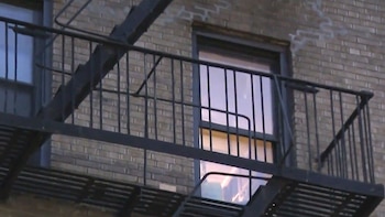 Primer plano de una escalera de incendios metálica negra adosada a la fachada de un edificio de ladrillo de color claro con ventanas