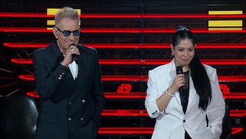Miguel Ángel Rodríguez con gafas oscuras y saco negro junto a Vanesa vestida de blanco, ambos con micrófonos en un escenario con luces rojas