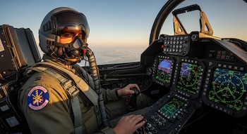 Piloto de combate con casco y máscara de oxígeno en la cabina de un avión militar. Se ven las pantallas de vuelo y el cielo sobre las nubes al fondo.