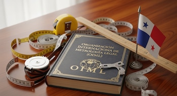 Un libro con el título Organización Internacional de Metrología Legal, varias cintas métricas, una regla de madera y una bandera de Panamá sobre una mesa.