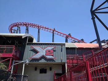 Cartel con la sigla X2 en la fachada de una edificación junto a rieles rojos de montaña rusa sobre soportes grises