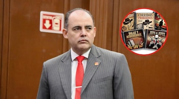 Primer plano de un hombre con traje gris y corbata roja mirando a la derecha, con un letrero de extintor detrás y discos de narcocorridos en la esquina superior derecha.