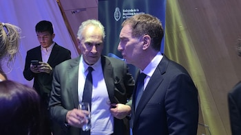 Dos hombres trajeados conversan frente a un panel de la Embajada de la República Argentina en Francia