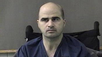 Un hombre calvo con camiseta azul oscuro permanece sentado delante de una pared de color gris
