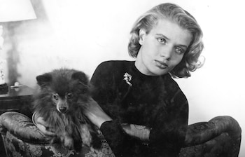 Imagen en blanco y negro de Chunchuna Villafañe, joven, con cabello ondulado claro, sentada en un sofá con un perro peludo y oscuro en sus brazos, mirando a cámara