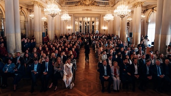Vista aérea de un gran salón ornamentado con columnas doradas y candelabros, donde una multitud de personas, incluyendo políticos y jueces, están sentadas