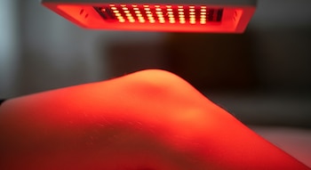 Dispositivo con múltiples luces LED rojas ilumina la piel de una rodilla.