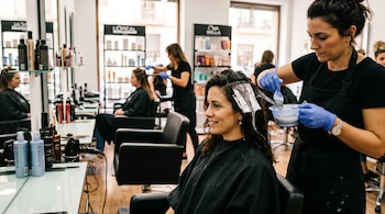 Una estilista con guantes azules aplica un producto con pincel en el cabello envuelto en papel de aluminio de una mujer.