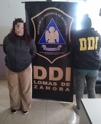 Un agente de espaldas con uniforme policial negro frente a un coche Volkswagen hatchback blanco y un cartel de la DDI Lomas de Zamora