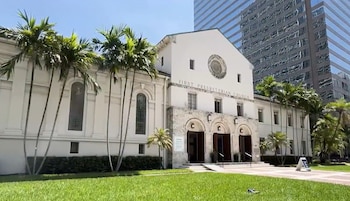 Fachada de la First Presbyterian Church, con palmeras y césped en primer plano. Un rascacielos de cristal se eleva en segundo plano