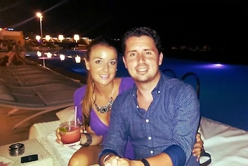 Maje Moreno Cantó y un hombre sonríen a cámara sentados en una zona de descanso junto a una piscina exterior por la noche. La mujer sostiene una bebida