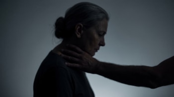 Perfil en sombra de una mujer mayor con el pelo recogido y la mano de una persona sobre su cuello.