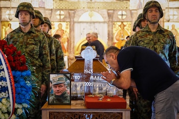Un hombre toca la cruz sobre el ataúd de Ratko Mladic en la iglesia de San Lucas, Belgrado. El funeral desafía las advertencias de la UE tras la muerte del criminal de guerra. (AP Photo/Marko Drobnjakovic)