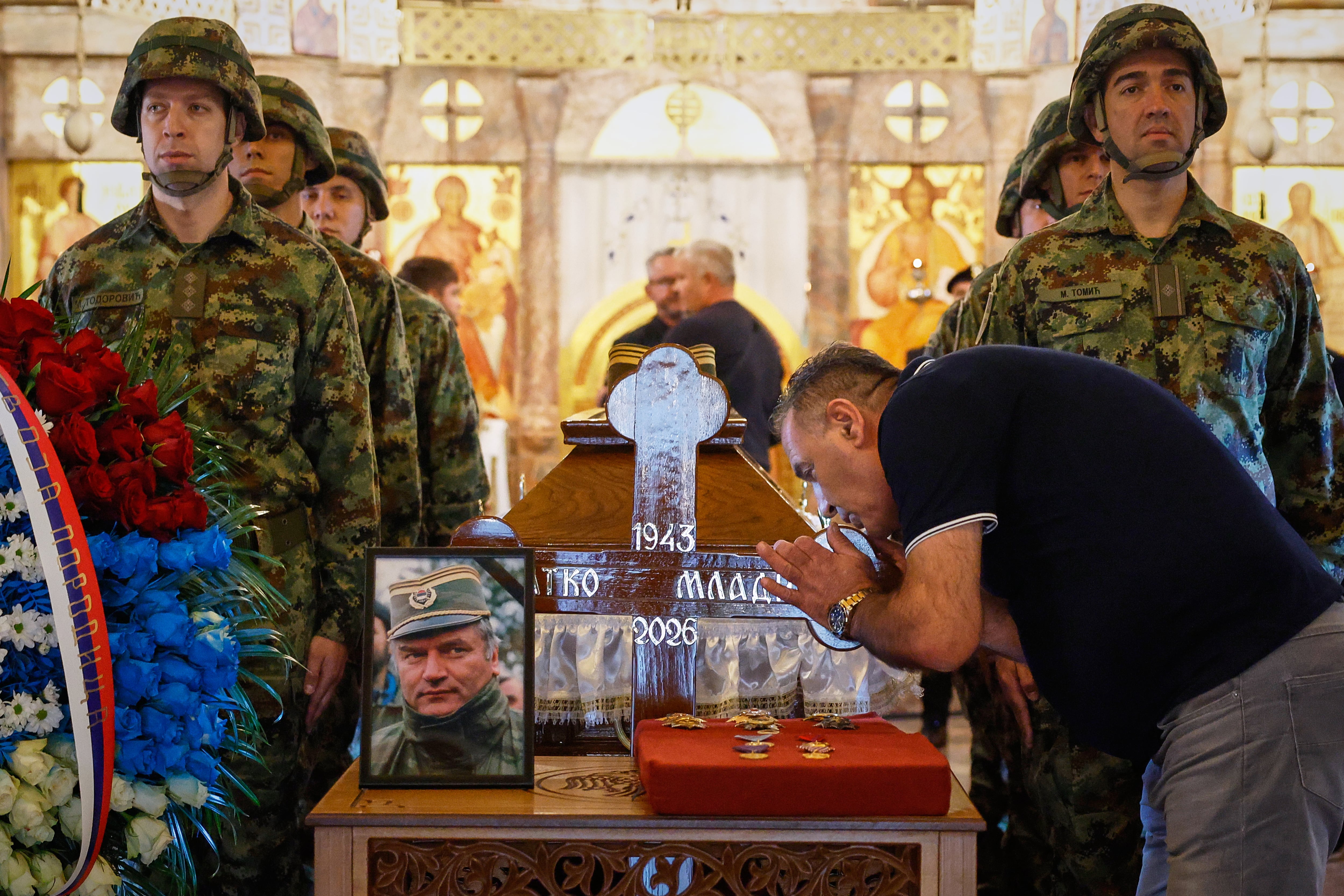 Un hombre toca la cruz sobre el ataúd de Ratko Mladic en la iglesia de San Lucas, Belgrado. El funeral desafía las advertencias de la UE tras la muerte del criminal de guerra. (AP Photo/Marko Drobnjakovic)