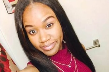 Primer plano de Kierra Coles, una mujer joven de piel oscura con cabello liso y oscuro. Viste un suéter fucsia y dos collares finos, mirando a la cámara