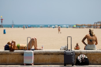 Unas turistas toman el sol junto a sus maletas en la playa de la Malvarrosa, a 13 de julio de 2026. (EFE/Ana Escobar)