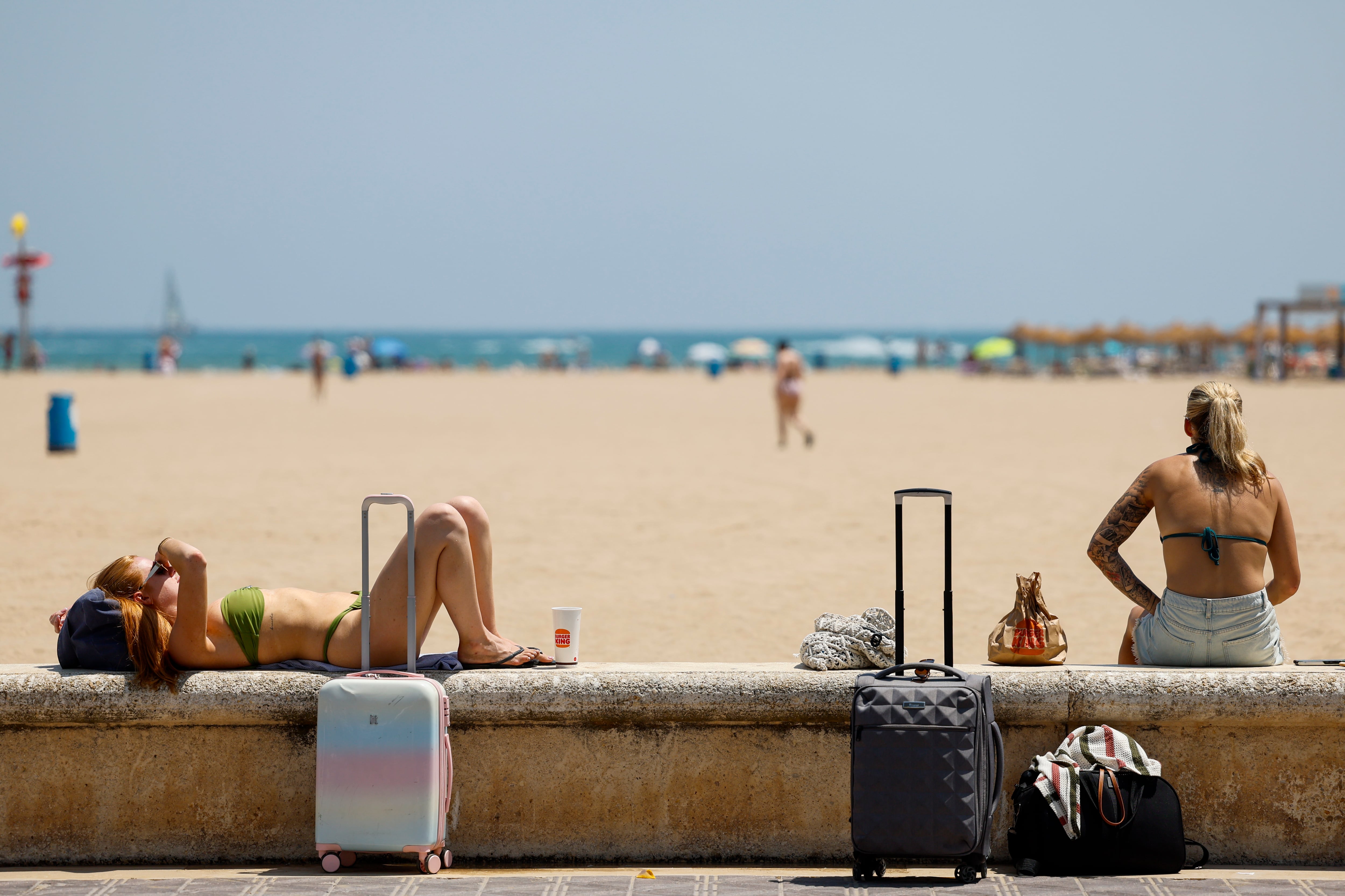 Unas turistas toman el sol junto a sus maletas en la playa de la Malvarrosa, a 13 de julio de 2026. (EFE/Ana Escobar)