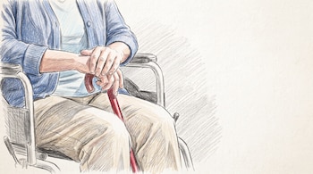 Cuerpo de una persona sentada en silla de ruedas, con chaqueta azul y pantalón beige, sujetando un bastón rojo con ambas manos.