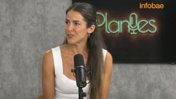 Mujer de cabello largo y camiseta blanca habla frente a un micrófono en un estudio con una pantalla de Infobae de fondo
