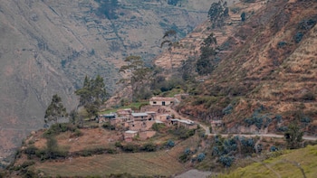 Casas pequeñas de adobe sobre la ladera de una montaña con vegetación seca y un camino de tierra en la sierra peruana