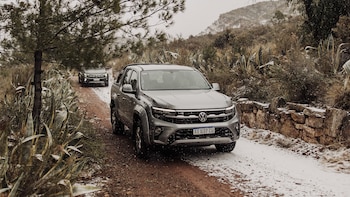 Dos camionetas pickup Volkswagen Amarok grises transitan por un camino de tierra nevado. Árboles, agaves y arbustos secos rodean el camino