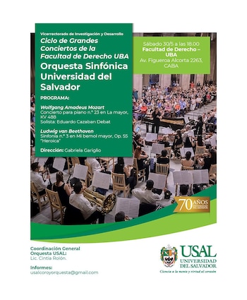 Una orquesta sinfónica tocando en un auditorio lleno de público. Se ven músicos con violines, vientos y un director frente a ellos