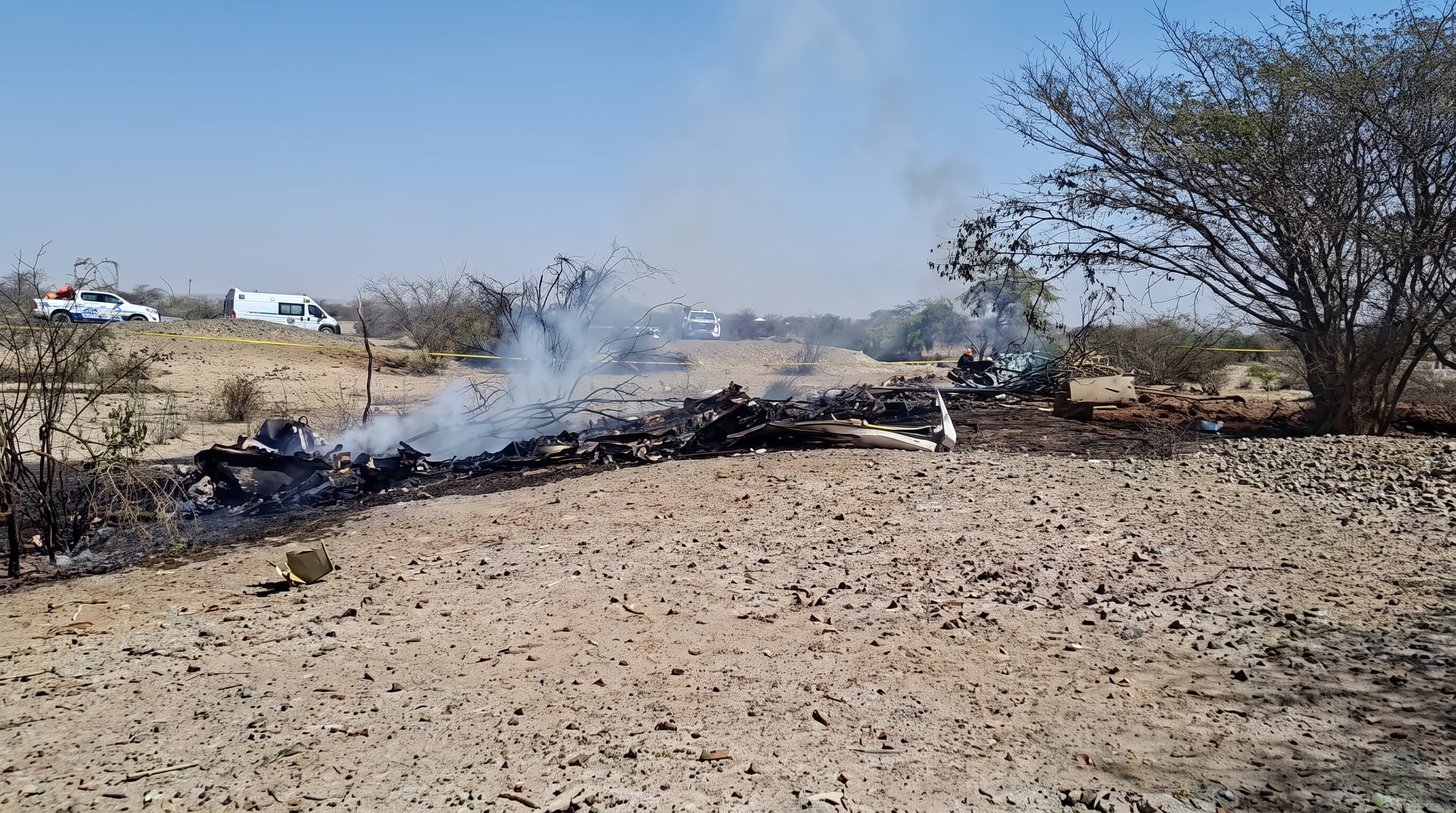 Escombros humeantes de una avioneta siniestrada y vehículos de emergencia se observan en un predio agrícola de Pueblo Viejo, Nasca, Perú, tras un accidente.