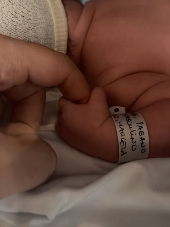 Primer plano de la mano de un bebé recién nacido que agarra el dedo de un adulto. El bebé lleva una pulsera de identificación en la muñeca