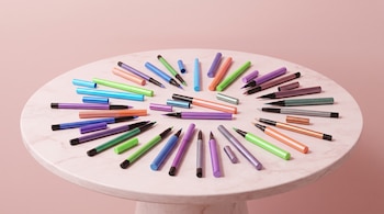 Delineadores de colores variados con y sin tapa ordenados en una mesa redonda de mármol sobre un fondo rosa.