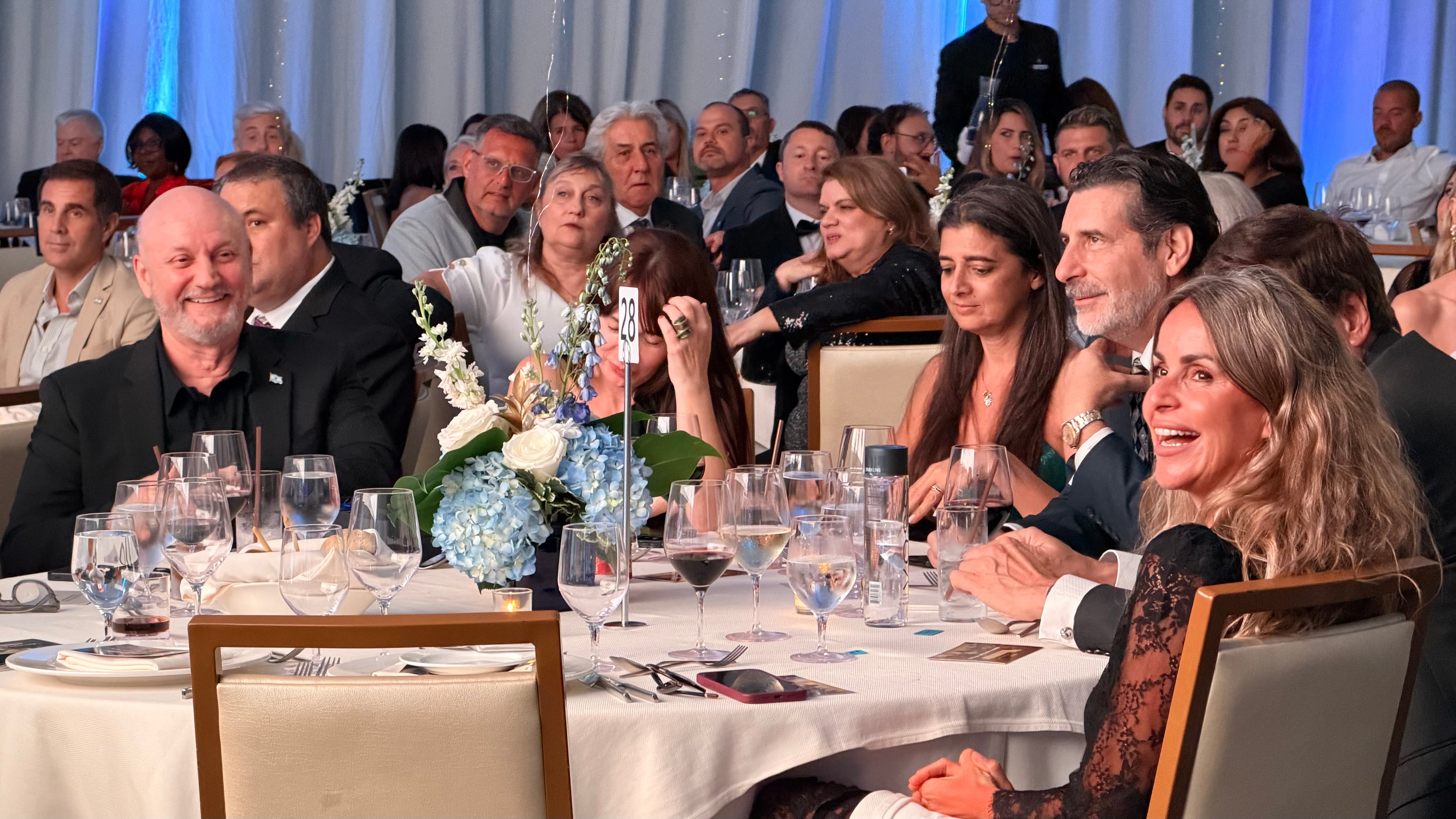 Juan José Campanella y Roberto Macho disfrutan de la cena durante la exitosa gala anual de la Cámara Argentino-Americana de Comercio, celebrada en Miami para fortalecer los lazos comerciales y de inversión.
